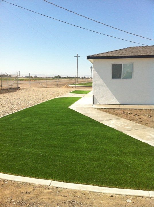Neatly landscaped yard with bright green artificial grass beside a white house under a clear blue sky