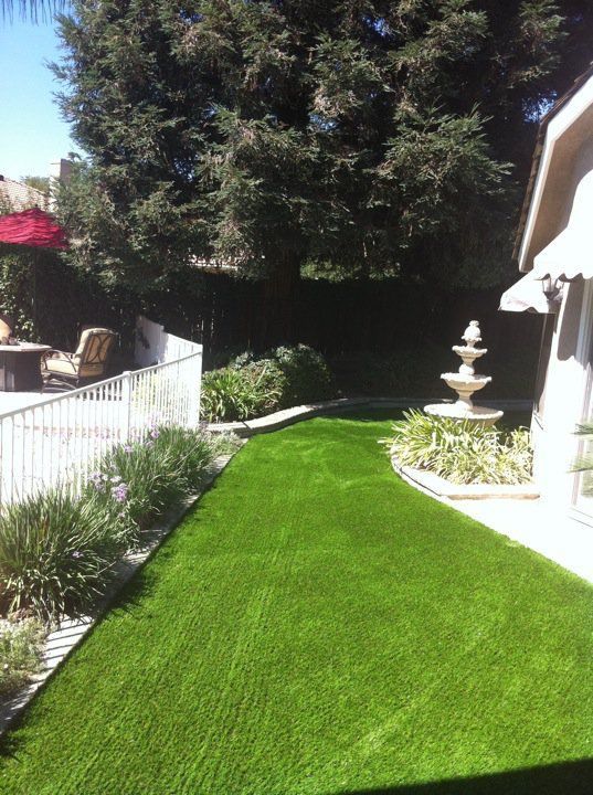 Sunny backyard with bright green lawn, white fence, and a small fountain beside the house