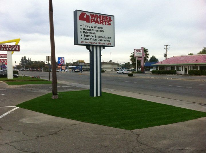 Roadside sign for 4 Paws Grooming along a street with businesses and a sidewalk.