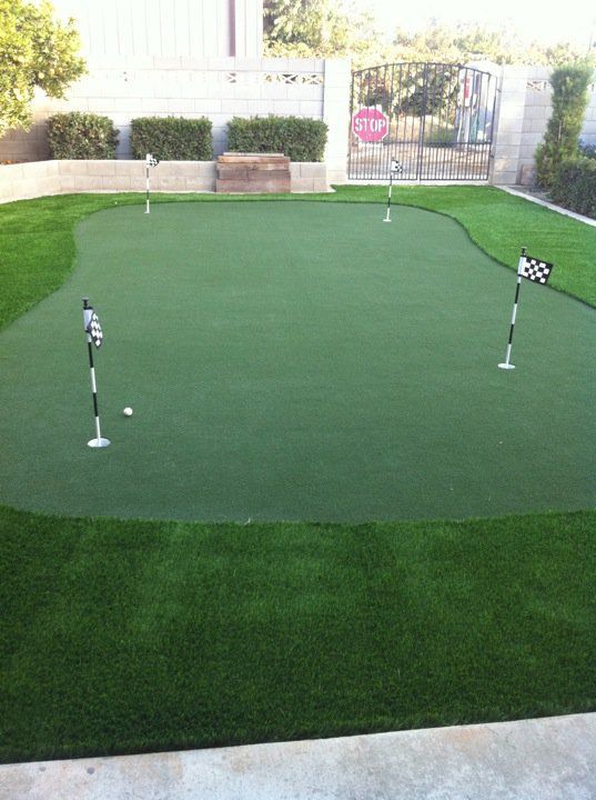 Small backyard putting green with three golf hole flags and a checkered flag on the right