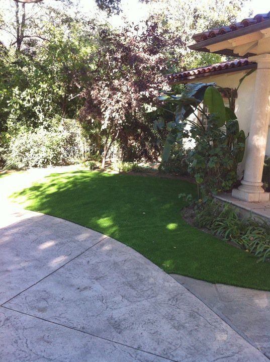 Sunny front yard with green lawn, concrete walkway, trees, and a stucco house with a columned porch