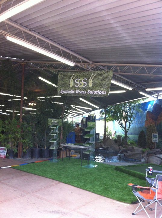 Covered outdoor café with green lawn, hanging sign, and plants under a corrugated roof
