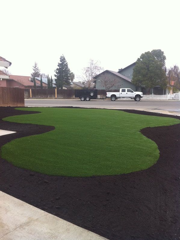 Curved green lawn bordered by dark mulch in a suburban front yard, with a white pickup truck on the street.