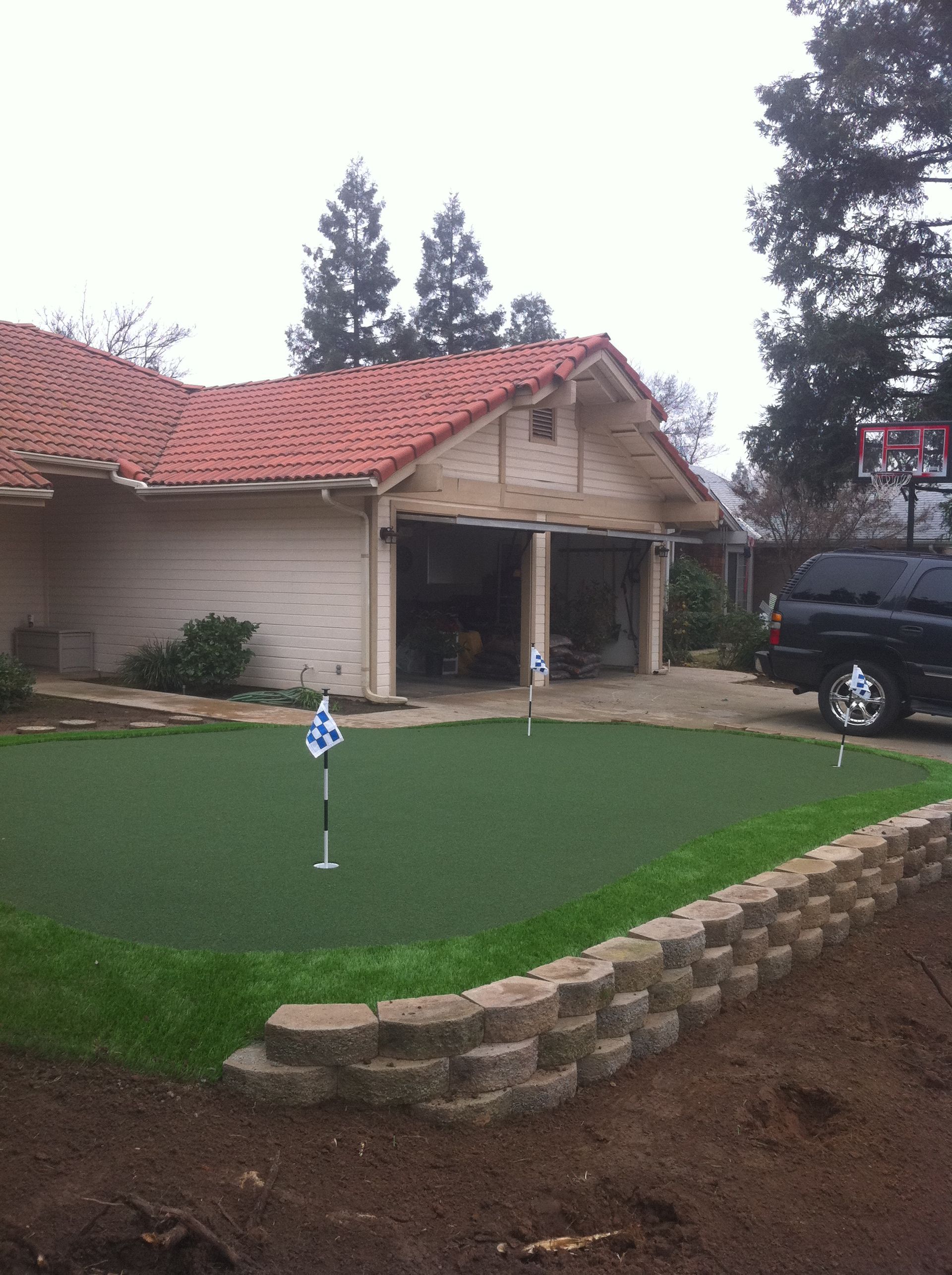 Suburban house with red roof, a small putting green in front, and a black vehicle parked beside it