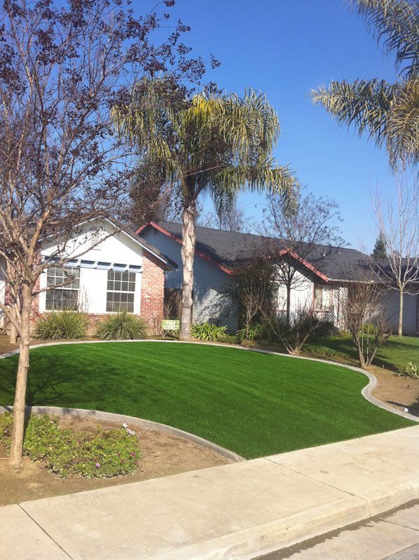 Suburban house with a manicured green lawn, trees, and a curved sidewalk under a blue sky