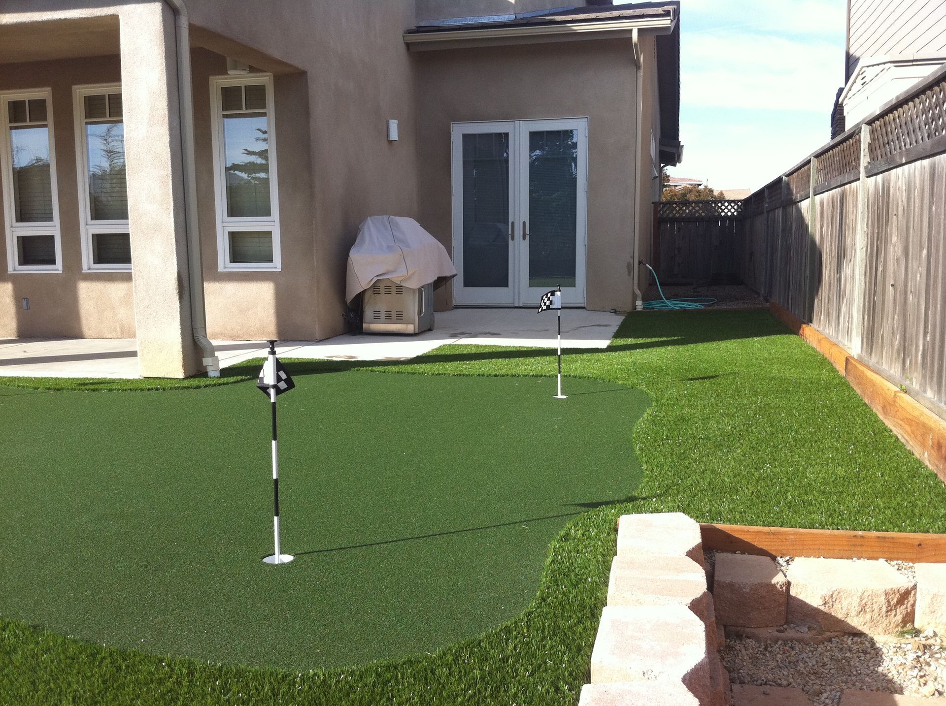 Backyard putting green with hole flags beside a house and wooden fence