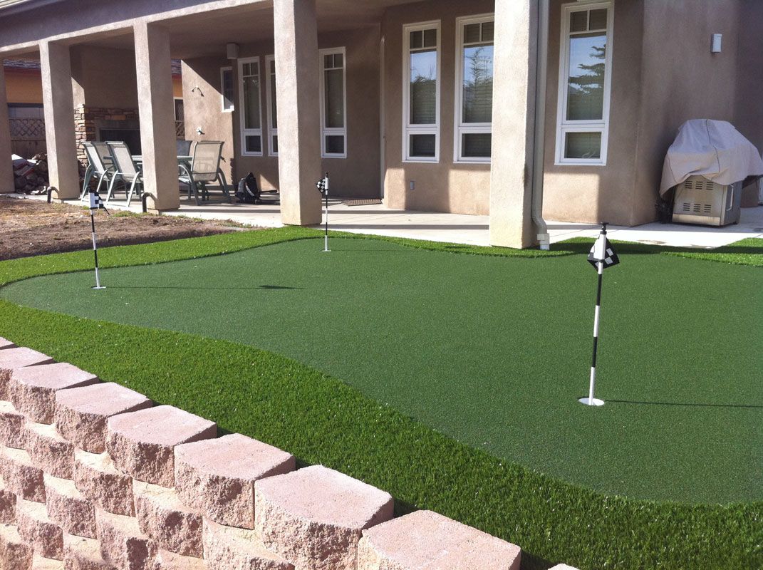 Green artificial turf courtyard beside a beige building with patio posts and small ground lights