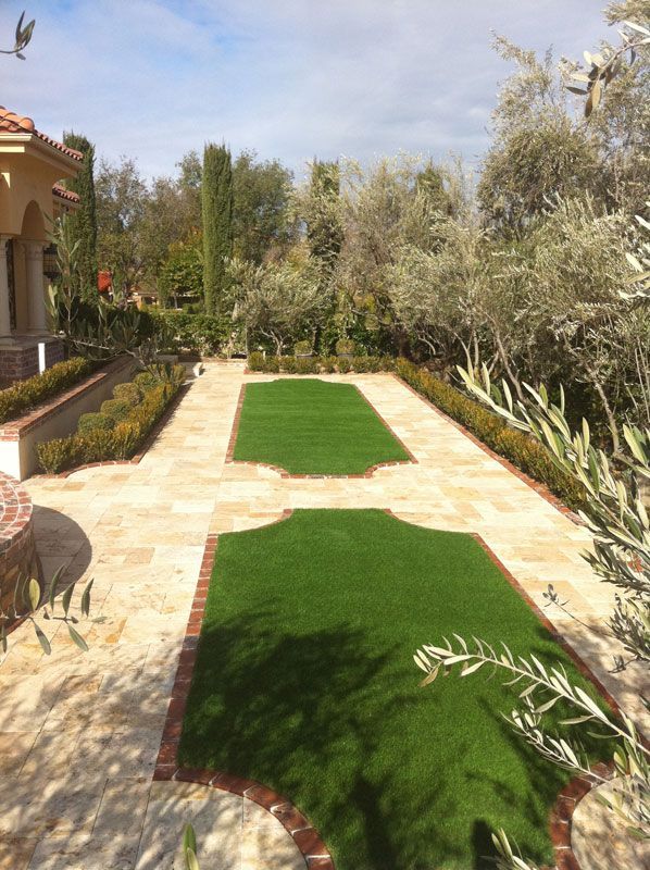 Stone walkway with green artificial grass strips in a landscaped garden beside a house