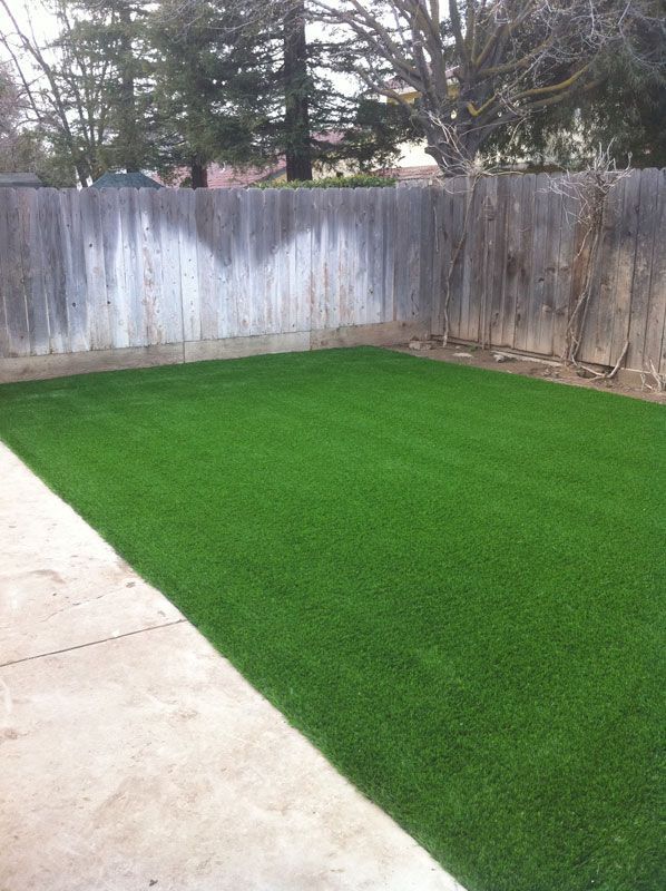 Backyard with fresh green artificial turf beside a concrete patio and weathered wooden fence