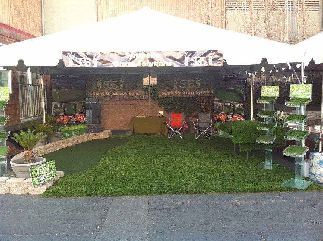 Covered outdoor patio with green turf, chairs, and stacked plant stands, viewed from the front.