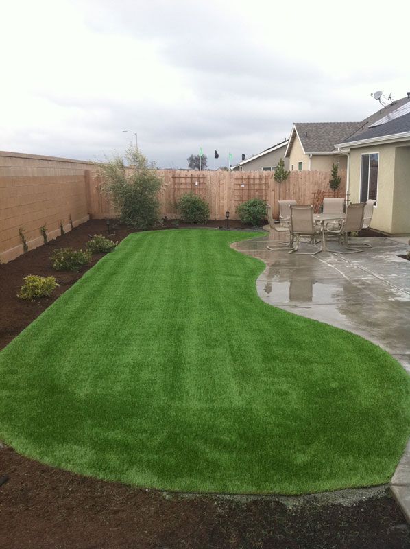 Freshly landscaped backyard with bright green sod, brown fence, and a wet concrete patio beside a house