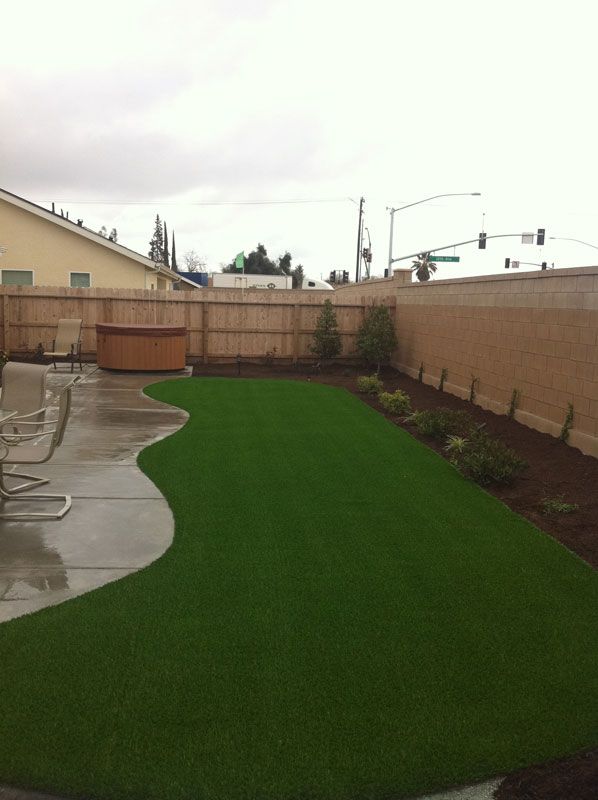 Backyard patio with bright green artificial turf and a wooden fence under overcast skies