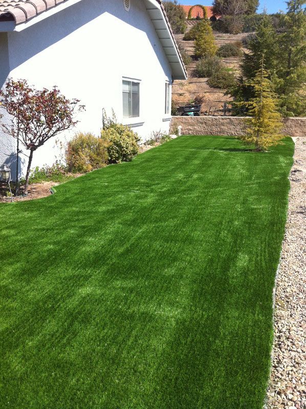 Freshly mowed green lawn beside a white house with a gravel path and landscaped hillside