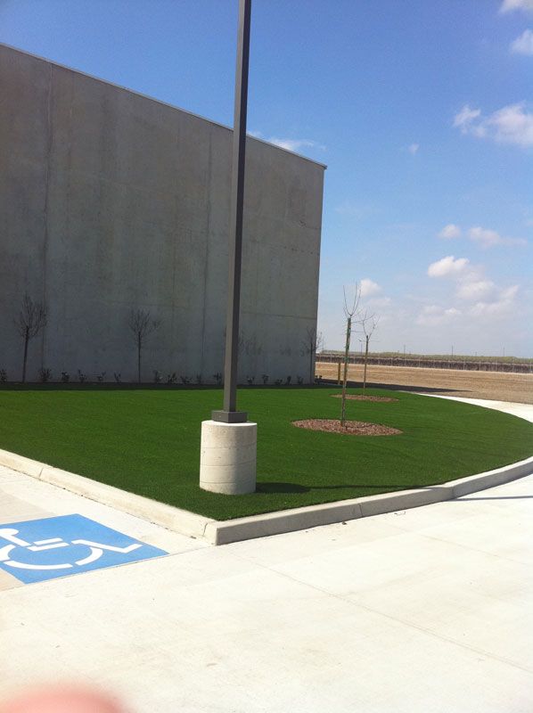 Parking lot beside a large building with a light pole, green grass, and a handicapped parking space mark