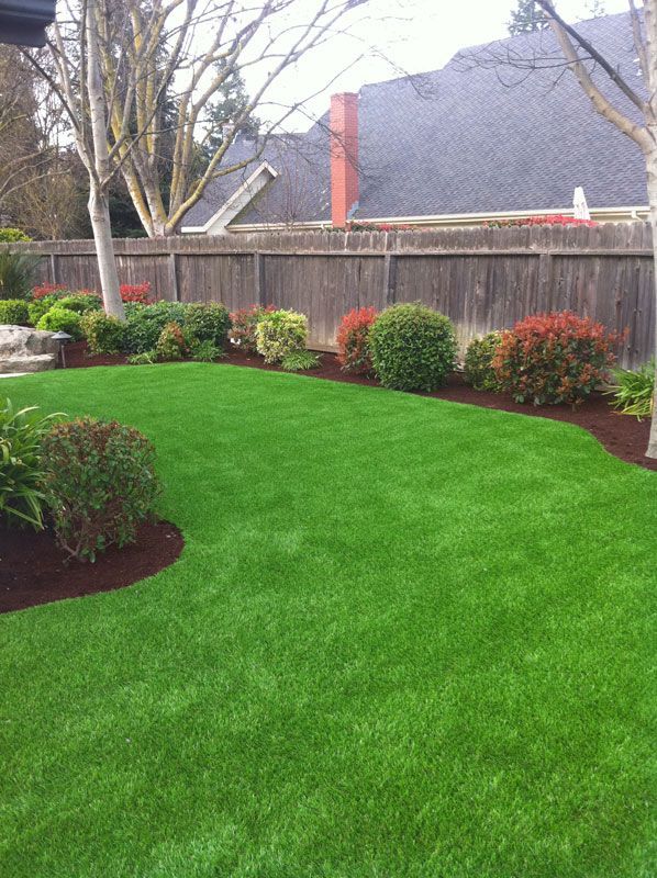 Well-manicured green backyard lawn with shrubs, mulched flower beds, and a wooden fence.