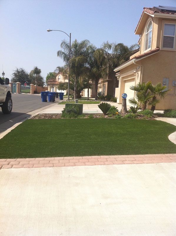 Suburban street with a manicured lawn, palm trees, and beige house under a clear sky
