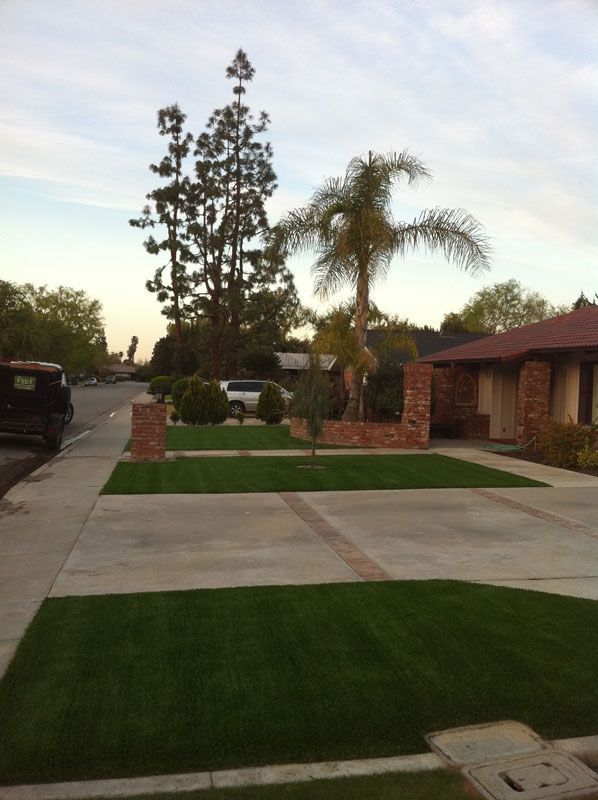 Suburban home with manicured lawn, driveway, palm trees, and brick entry at dusk