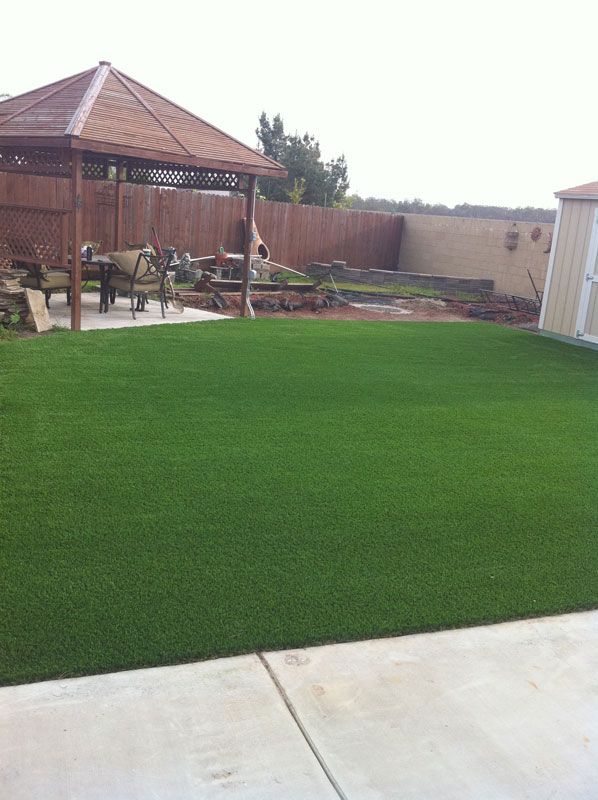 Backyard with bright green lawn, covered patio, and concrete walkway under a cloudy sky