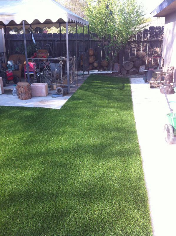Backyard with fresh green artificial turf, patio seating, and a shaded canopy area