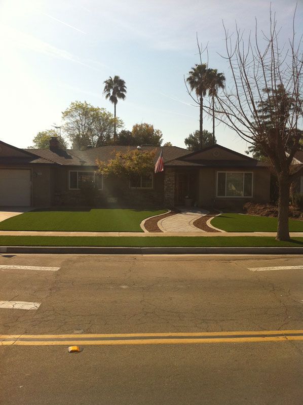 Single-story house with a manicured lawn, curved walkway, palm trees, and an American flag by the street.