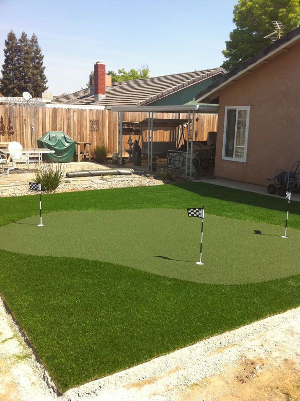 Backyard putting green with two flagsticks beside a house and wooden fence