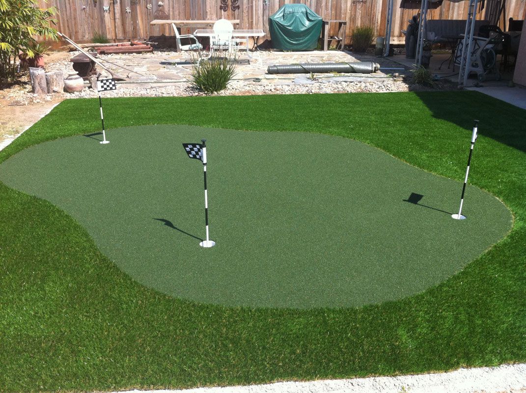 Backyard putting green with three golf flags on artificial turf