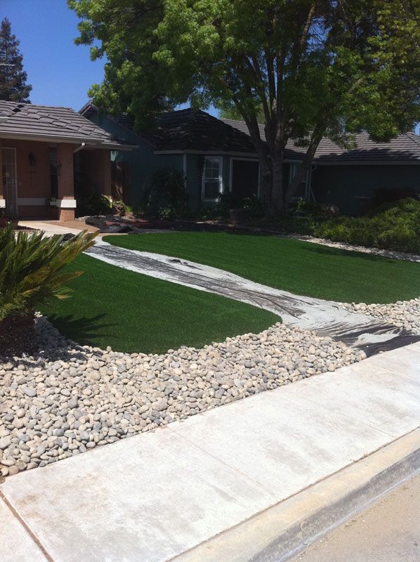 Suburban front yard with green lawn, rock border, and concrete walkway leading to a house