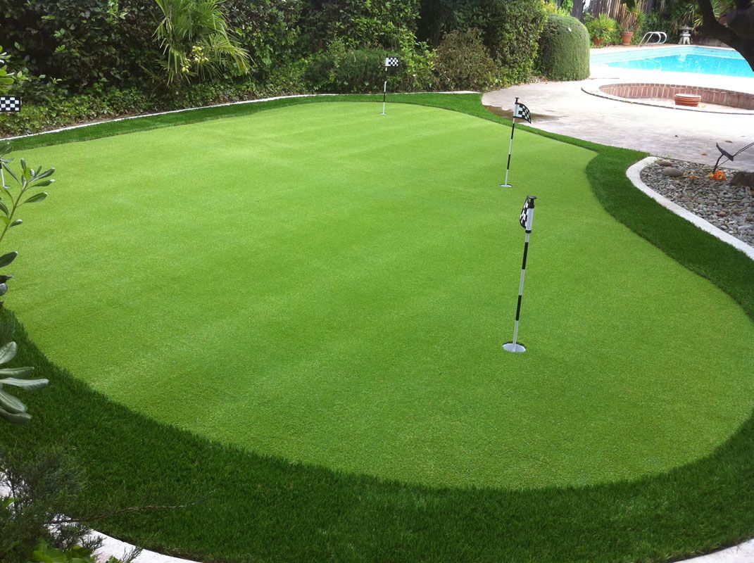 Manicured green lawn beside a pool, bordered by shrubs and a walkway, with a sprinkler in the center.