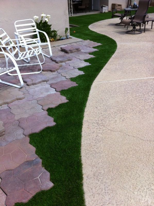 Curved garden path with pavers, grass border, and white patio chairs beside a house