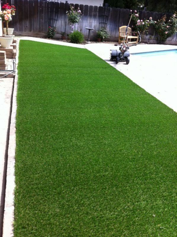 Backyard pool with bright green artificial turf and a small cleaning robot by the water