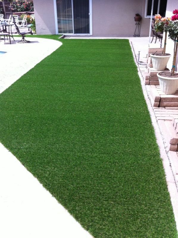 Green artificial turf walkway in a landscaped backyard beside a patio and potted plants.