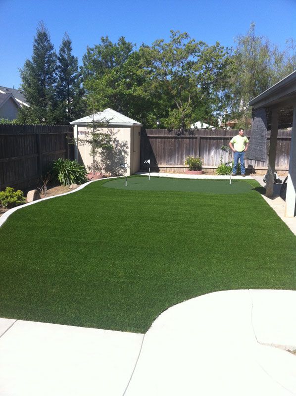 Backyard with fresh green artificial turf, white patio, shed, and a person standing near the fence