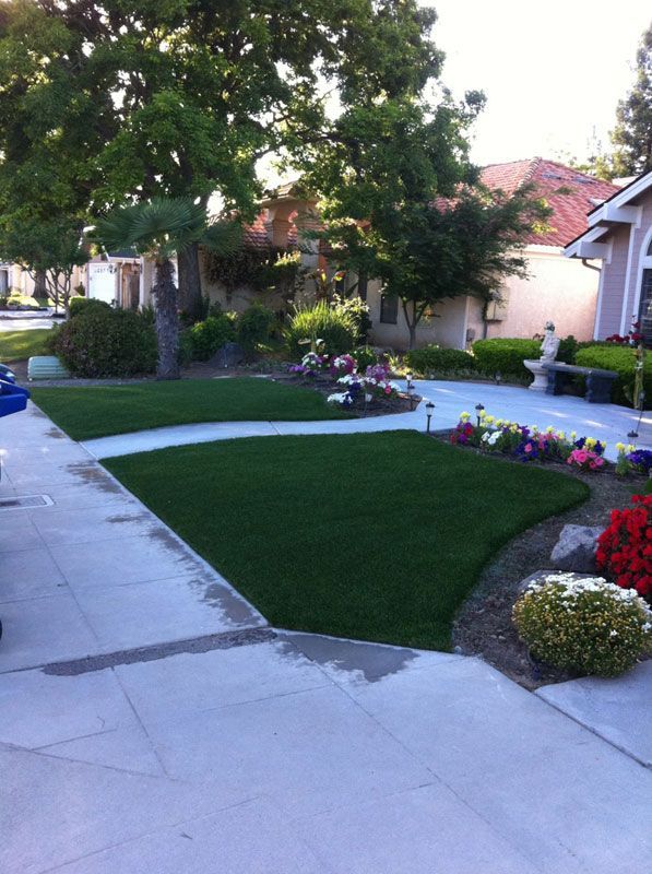 Suburban front yard with curved concrete walkway, green lawn, flower beds, and trees at dusk