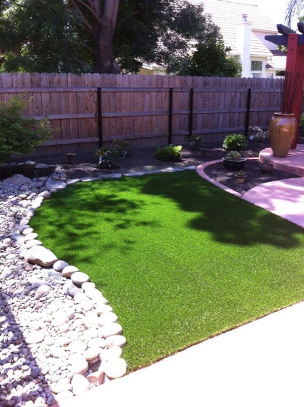 Backyard with artificial grass, stone border, and wooden fence in sunlight