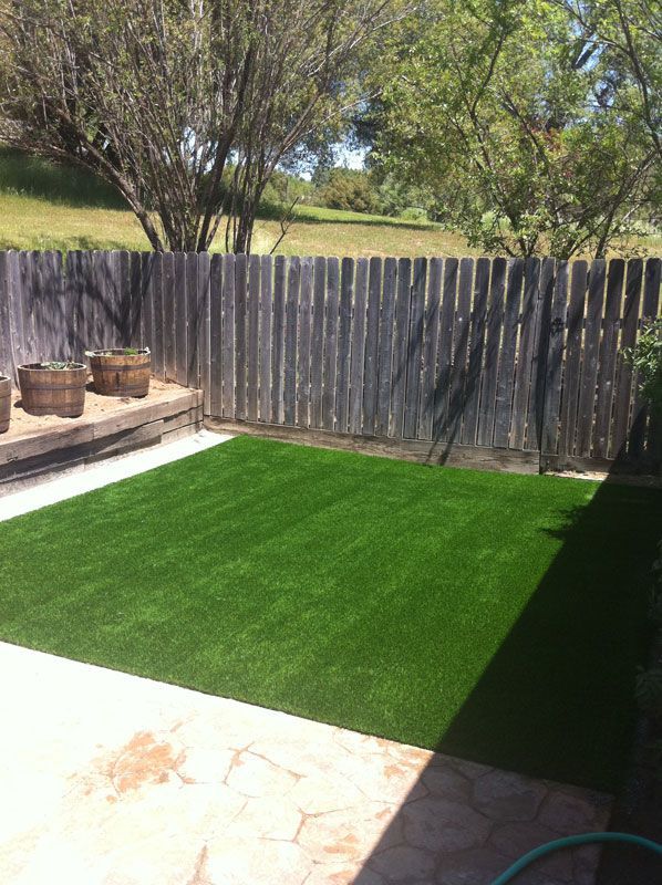 Backyard patio with bright green artificial turf, wooden fence, and potted plants in sunlight