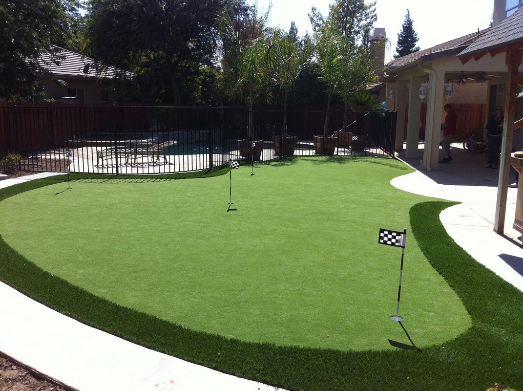 Backyard putting green with a flagstick, surrounded by trees and a patio