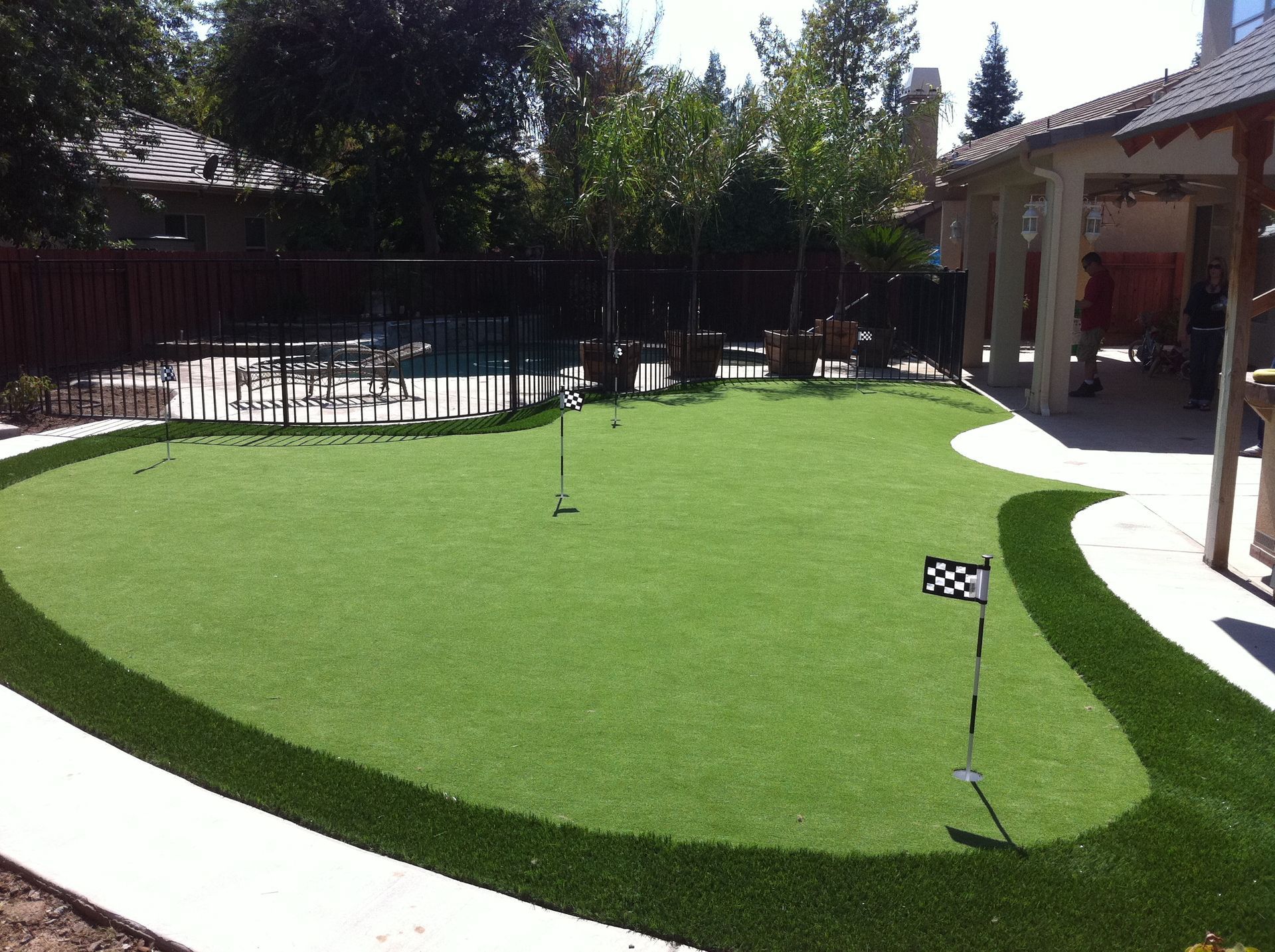 Small artificial turf putting green with two flags in a sunny backyard garden