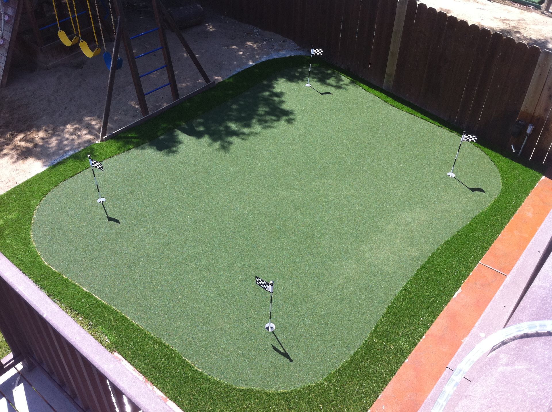 Synthetic turf putting green in a backyard with golf practice flags and cups