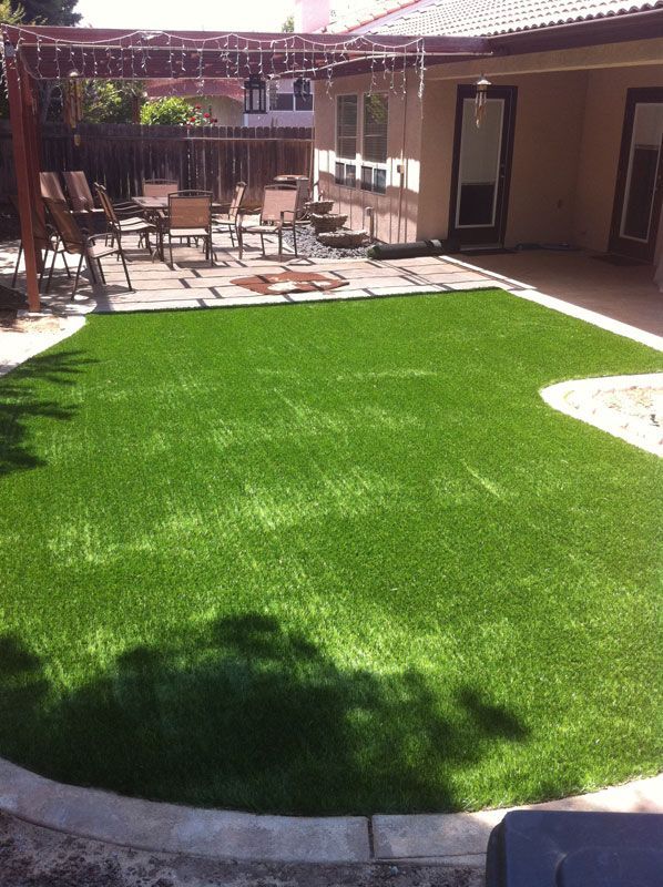 Backyard patio with bright green artificial lawn, outdoor chairs, and a shaded seating area.