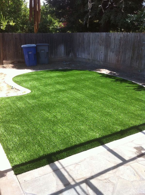 Backyard with bright green artificial turf, stone patio, and wooden fence in sunlight