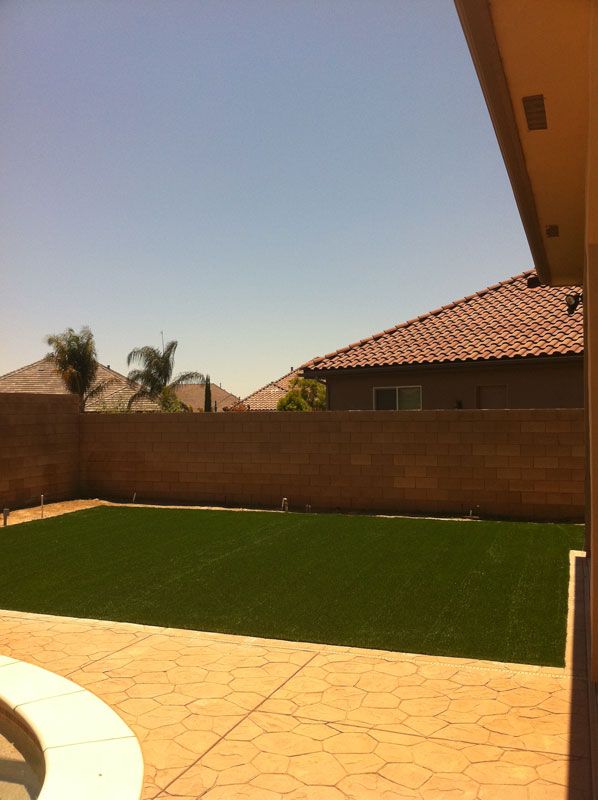 Backyard patio with green lawn, brick wall, and red-tiled roof under a clear sky