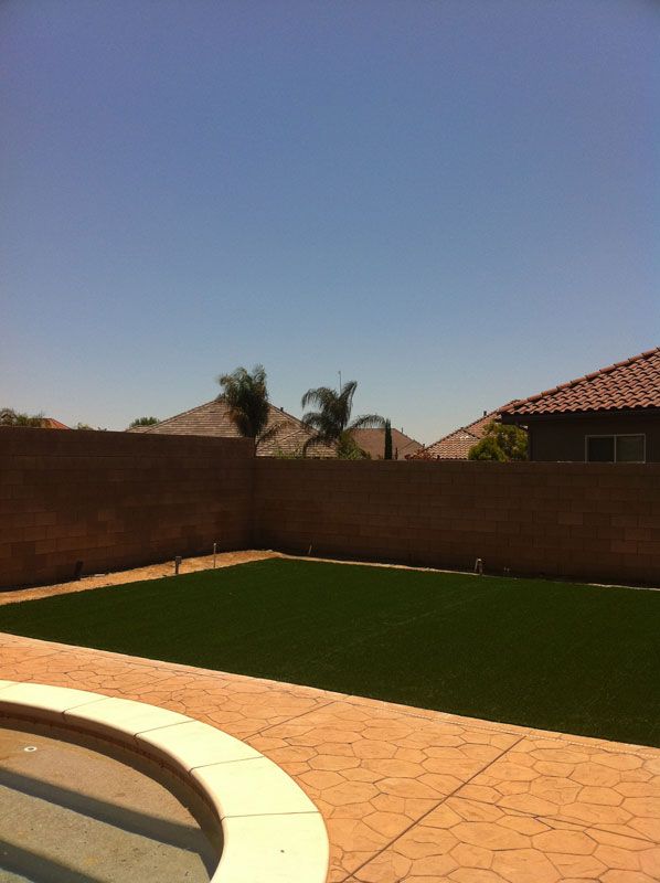 Backyard patio with artificial grass, brick wall, and tiled roof under a clear blue sky