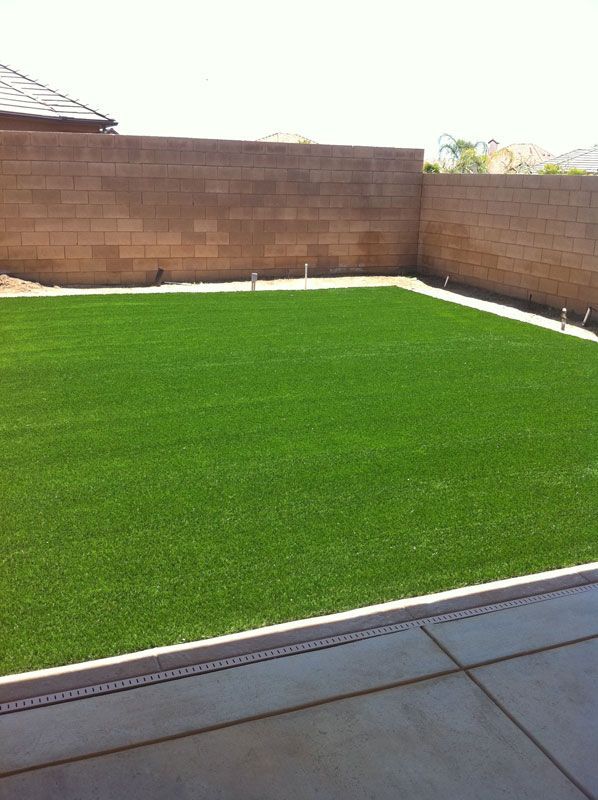 Backyard with bright green artificial turf, brick walls, and a concrete patio edge