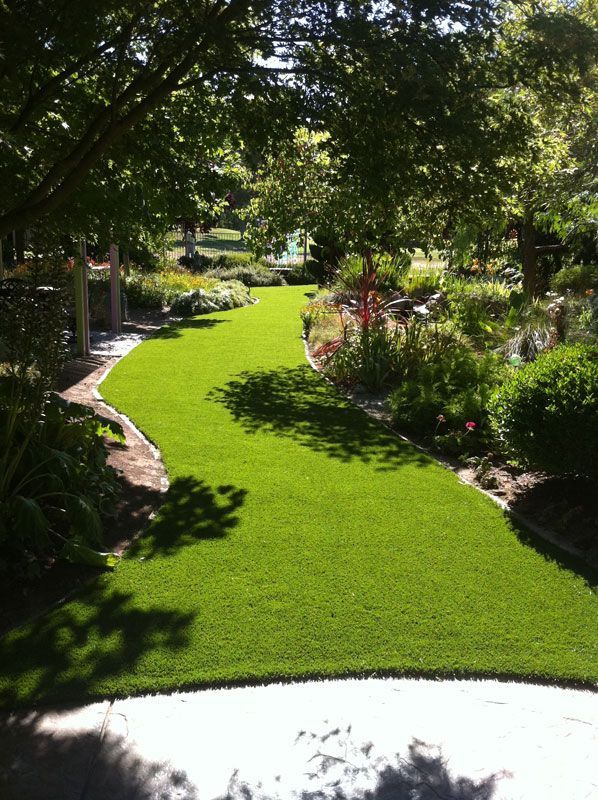 Lush green garden path bordered by trees, flowers, and rocks, leading into a sunny landscaped yard