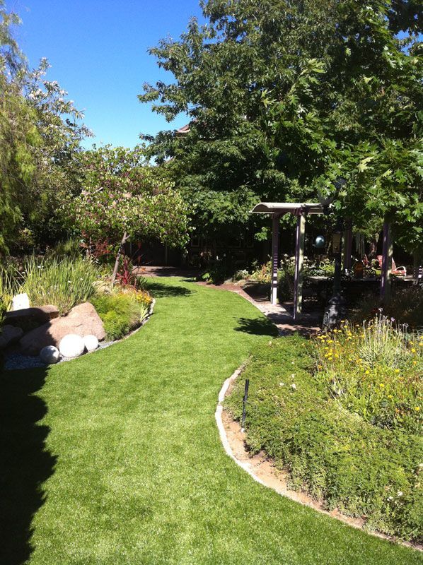 Sunny garden path with green lawn, flowering borders, and a small gazebo under trees
