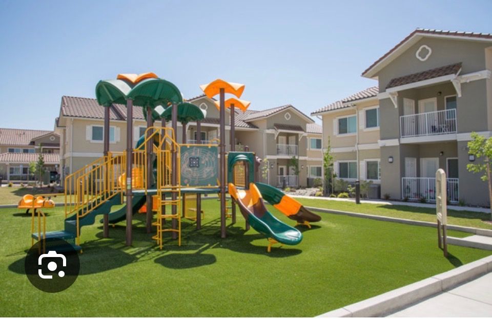Apartment courtyard with colorful playground on green turf and beige townhouse buildings.