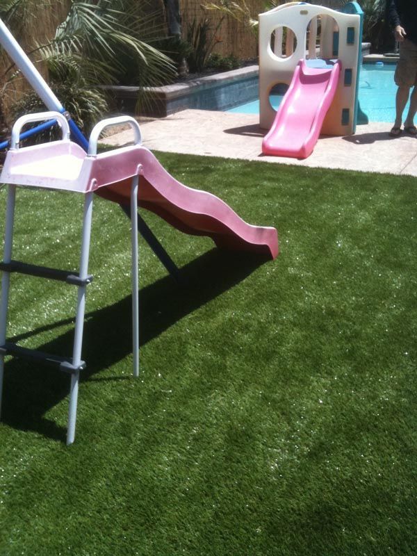 Children’s plastic slide with pink and white playground set beside a pool on green grass