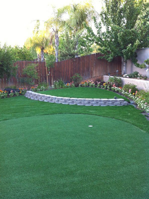 Backyard with green lawn, stone retaining wall, flower bed, and wooden fence at sunset