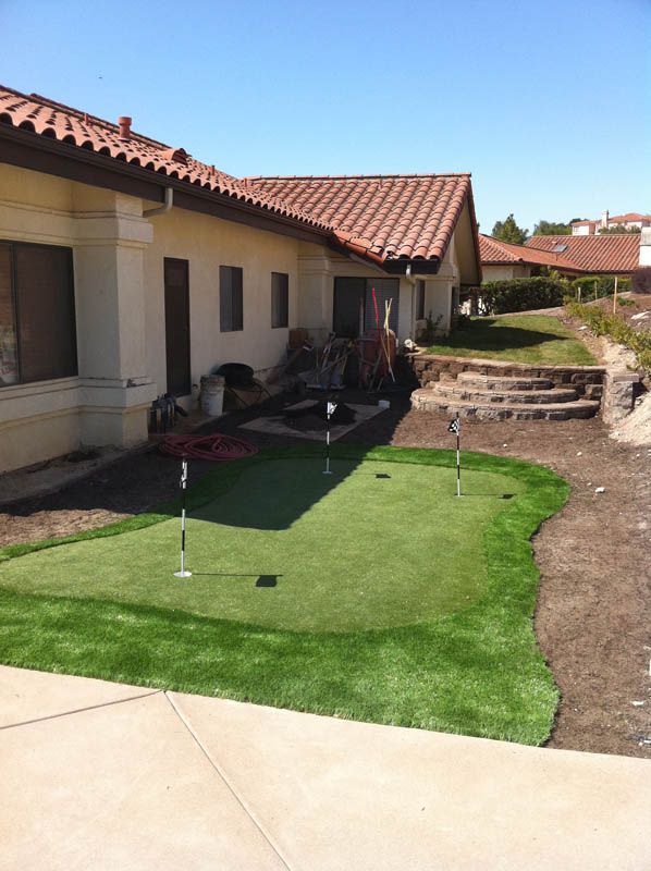 Courtyard outside a stucco house with a small lawn, potted plants, and a tiled roof on a sunny day