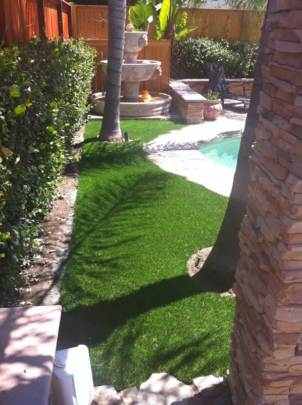 Tropical backyard with green lawn, palm tree, stone patio, and a small pool beside brick columns